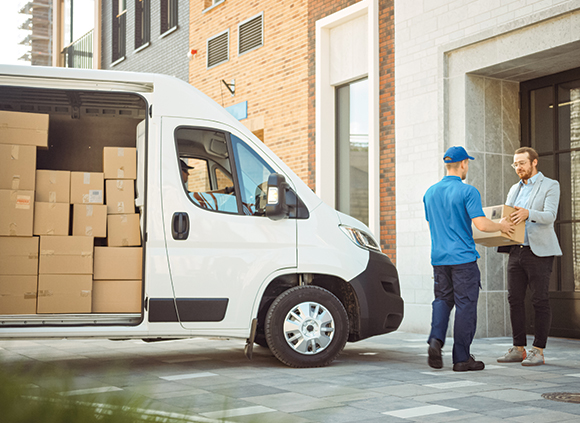 a courier handing a parcel to an employee of a business next to a van of parcels